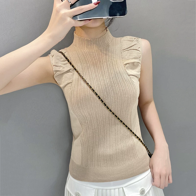 Angled view of beige high-neck ribbed knitted top styled with white skirt
